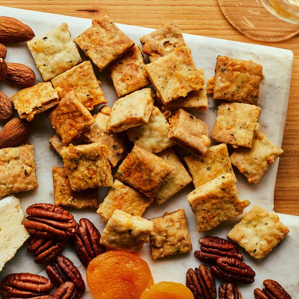 Une planche apéro garnie de craquelins au fromage, raisins frais, abricots secs, noix et brie. 