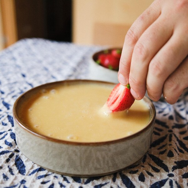 Un bol de crème anglaise et une main qui y plonge une fraise.