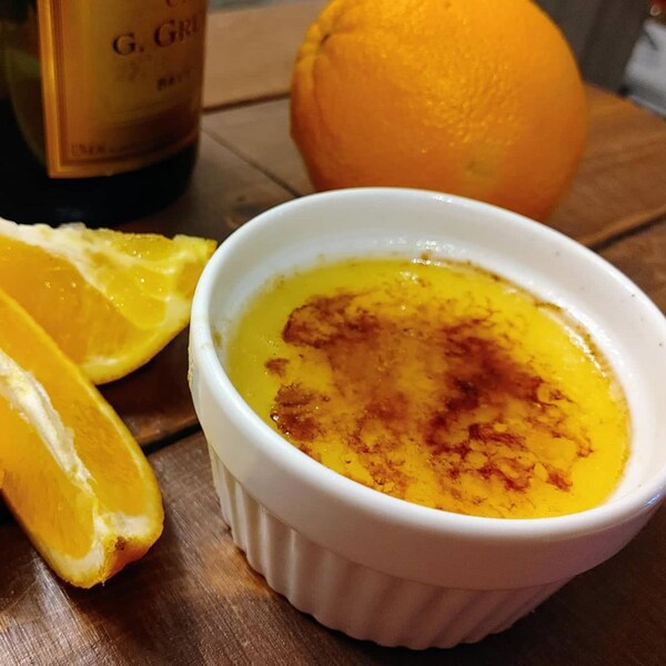 Un ramequin contenant une crème brulée accompagnée de quartiers d'orange.