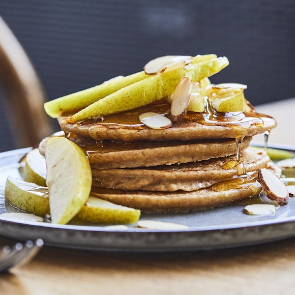 Une pile de quatre crêpes dans une assiette avec des morceaux de poires, d'amandes et du sirop d'érable.
