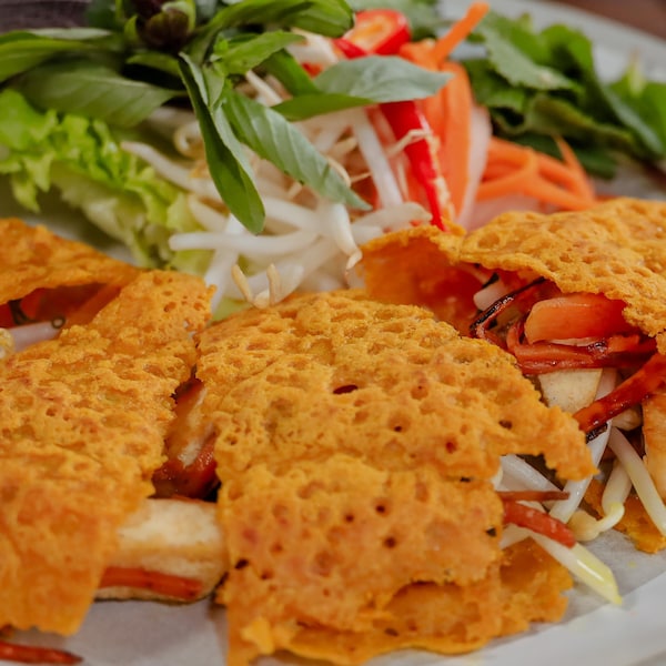 Des tranches de crêpes vietnamiennes farcies, accompagnées d'herbes fraîches, de légumes marinés et de fèves germées.