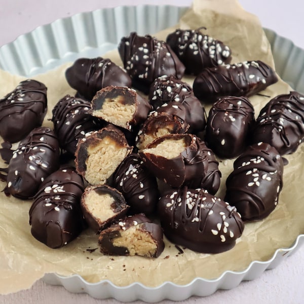 Des dattes farcies et enrobées de chocolat servies dans une assiette à tarte tapissée de papier parchemin.