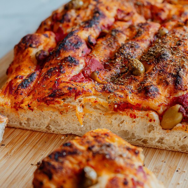 Une foccacia aux tomates et aux olives sur une planche à découper.