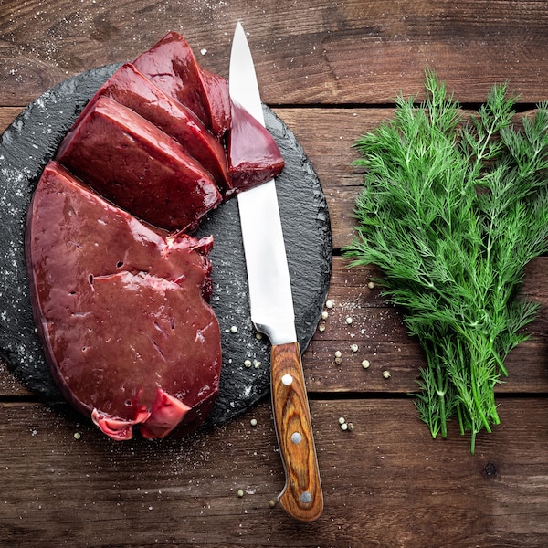 Un foie de veau en morceau sur une planche avec un couteau et  un bouquet d'aneth.