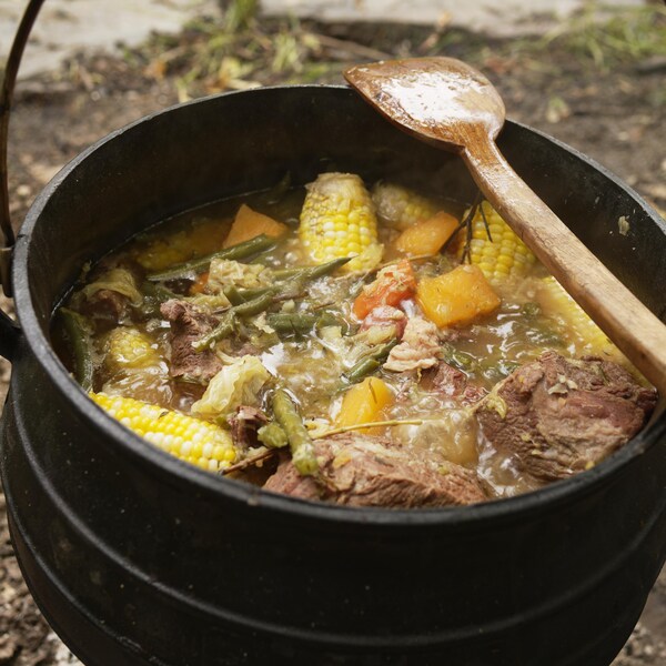 Une casserole  en fonte au-dessus d'un feu contient des morceaux de viande et des légumes cuits.