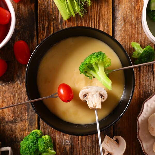 Un bol rempli de fondue au fromage avec des brocolis, des pommes de terre, des champignons et des petites tomates dans des bol à part.