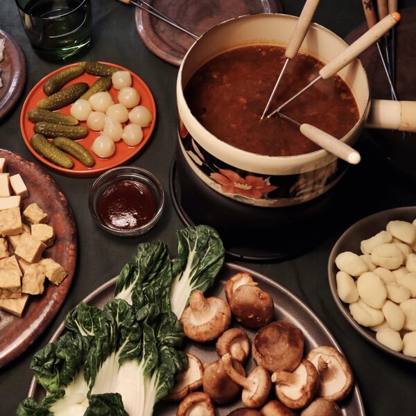 Un caquelon rempli de bouillon à fondue, avec plusieurs aliments à tremper dans le bouillon tels que : des champignons, du tofu, du tempeh, des gnocchis et des bok choys.