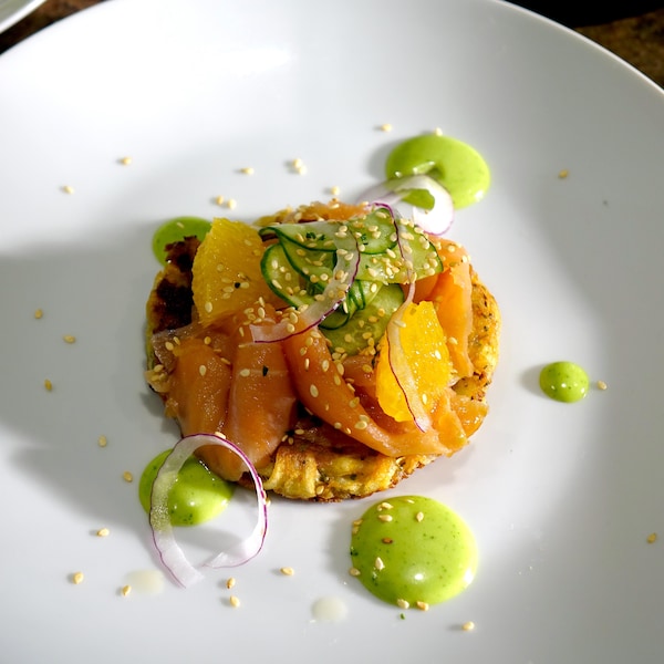 Une galette de pommes de terre recouverte de saumon fumé, de concombre et d'orange avec une mayonnaise au wasabi.