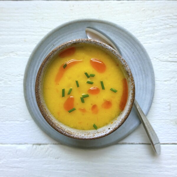 Un gaspacho jaune dans un bol déposé dans une petite assiette bleue.