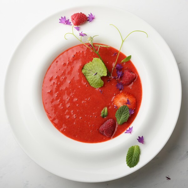Un bol de gaspacho au melon d'eau et aux tomates garni de fraises et d'herbes fraîches.