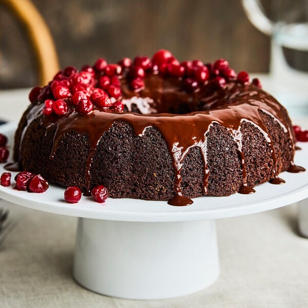 Un gâteau au chocolat et aux canneberges sur un présentoir à gâteau blanc sur pied.