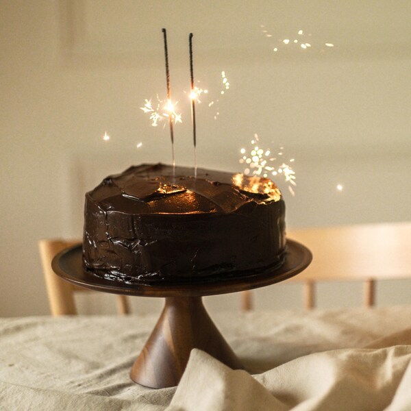 Un gâteau au chocolat sur un porte-gâteau, avec des chandelles allumées.