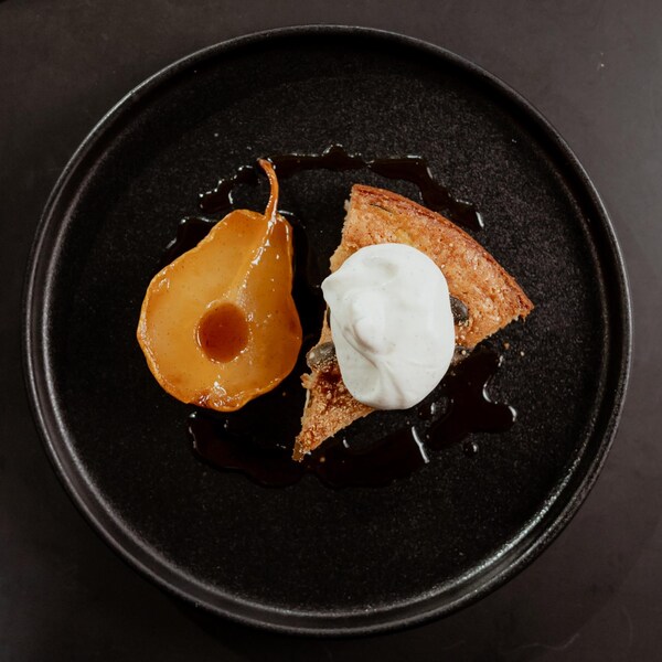 Une pointe de gâteau recouverte de crème fouettée et accompagnée d'une poire rôtie à l'érable.