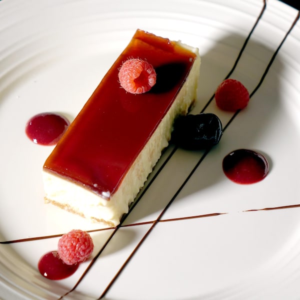Un morceau rectangulaire de gâteau au fromage décoré avec quelques framboises.