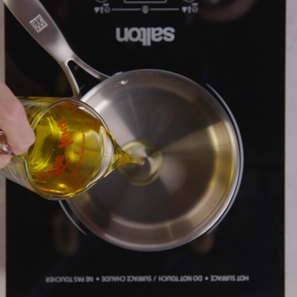 Une personne verse dans une casserole de l'huile de tournesol. 