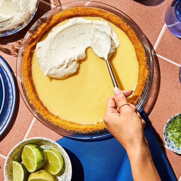 Une personne étend de la crème fouettée sur une tarte à la lime.
