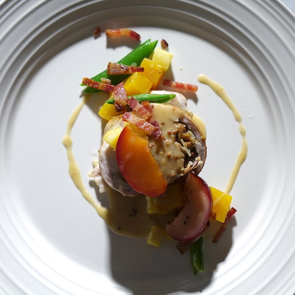 Un morceau de lapin rôti accompagné de prunes marinées et de quelques légumes et fruits.