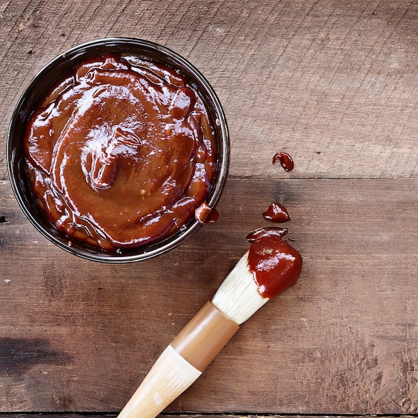 Un pot de sauce barbecue avec un pinceau dont le bout est recouvert de sauce.