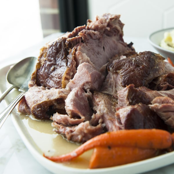 Un jambon en tranches dans un plat de service, avec des carottes et de la purée de pommes de terre.