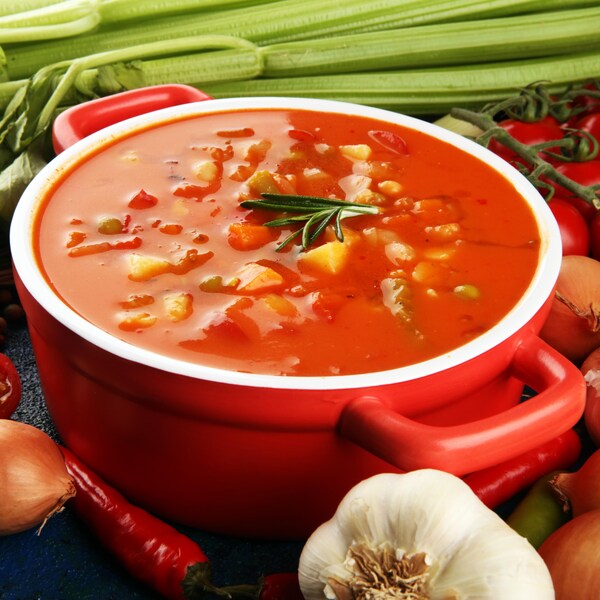Un bol rempli de soupe minestrone et entouré de plusieurs légumes.