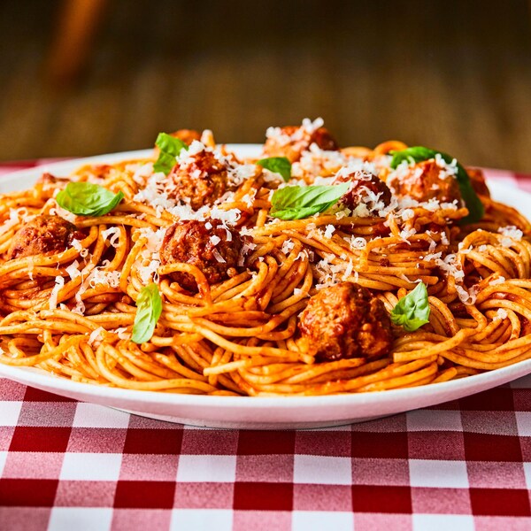Une assiette de spaghetti aux boulettes sur une table avec une nappe à carreaux. 