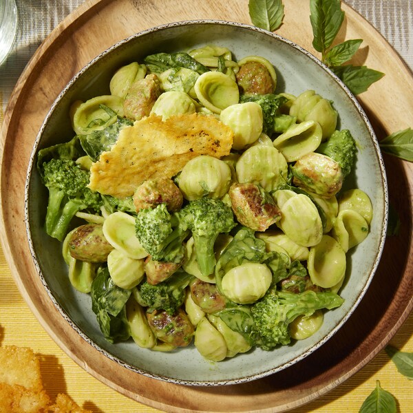 Un bol contenant des orecchiettes au brocoli, saucisses italiennes et servi avec une tuile de parmesan.