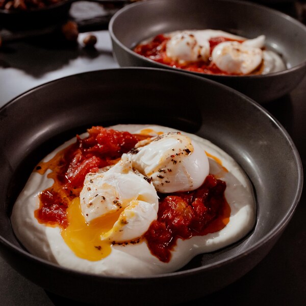 Deux œufs pochés sur du yogourt à l'ail et un concassé de tomates.