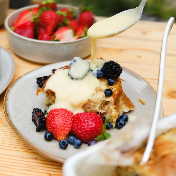 Du pain perdu dans une assiette recouvert de petits fruits et de crème anglaise.