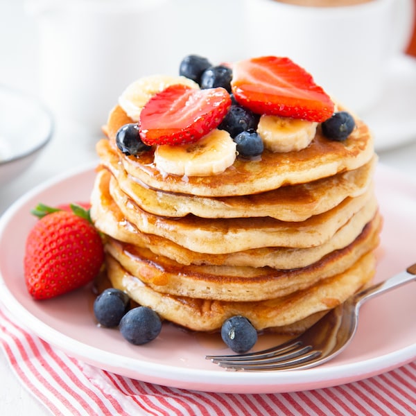 Des pancakes dans une assiette avec des bleuets, des fraises et des bananes.