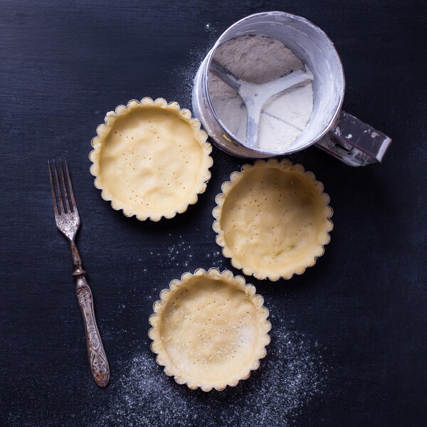 Des moules à tartelettes foncés avec de la pâte sucrée.