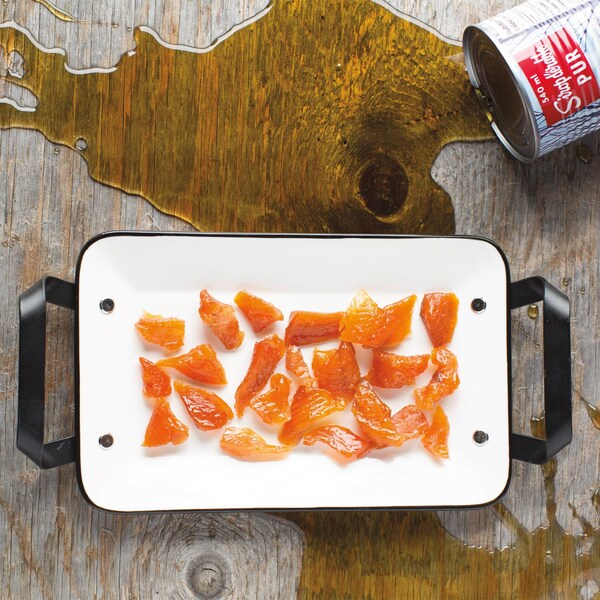 Un plat rectangulaire contient des morceaux de truite marinée à côté d'une canne de sirop d'érable renversée.