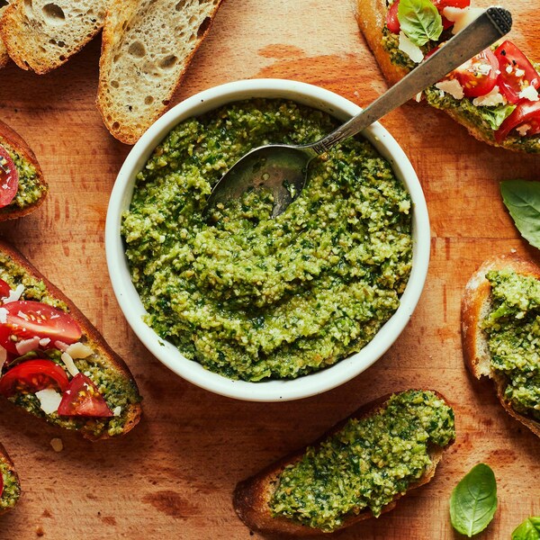 Un bol contenant le pesto antigaspillage aux queues d’asperges au centre d’une planche de bois. Il y a des croûtons garnis de pesto, de tomates et de fromage autour du bol.