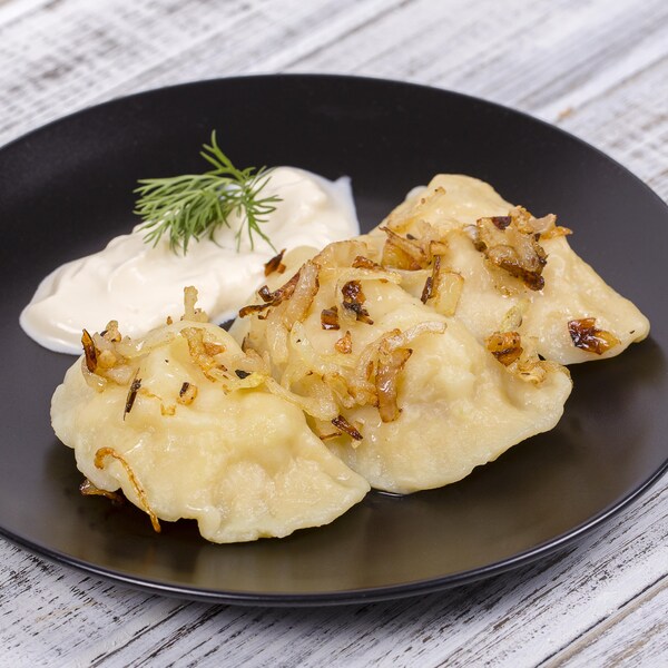 Des pierogis accompagnés de crème sure dans une assiette.