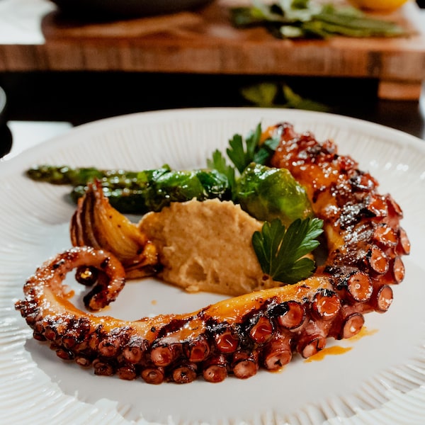 Un tentacule de pieuvre laquée dans une assiette avec des légumes verts et de la purée de châtaignes.