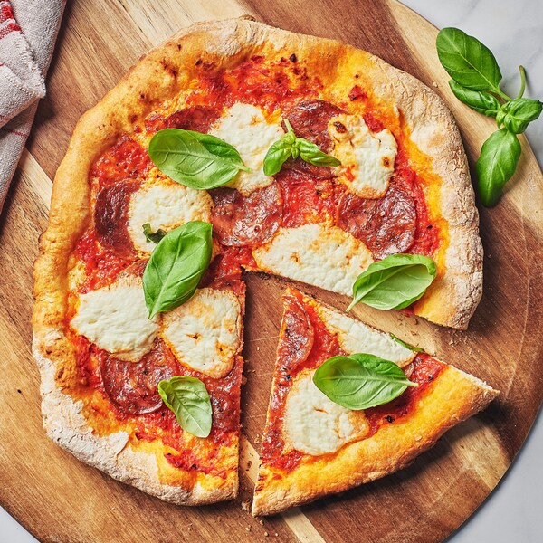 Une pizza à croute mince au fromage frais sur une planche à découper.