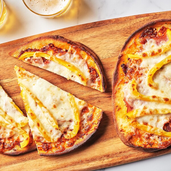 Des pizzas sur pains naans au capicollo et au poivron servies sur une planche de bois.