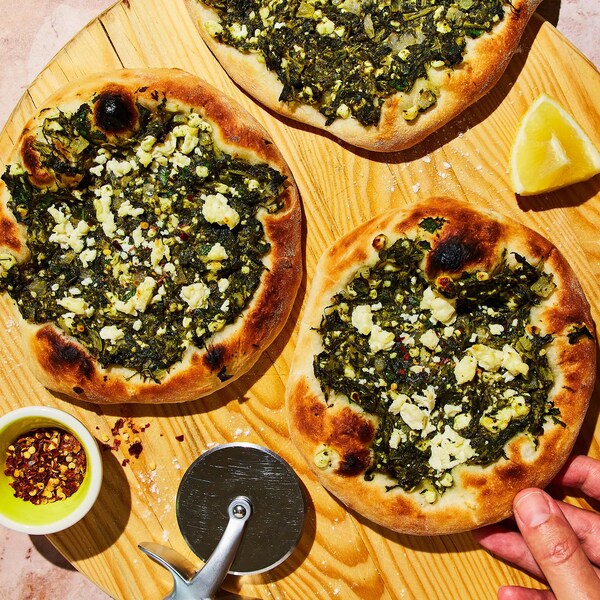 Trois pizzas spanakopita sur une planche de service.