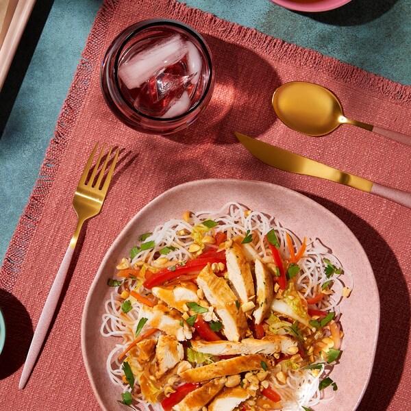 Une assiette contenant des vermicelles de riz, des légumes sautés et du poulet cuit.