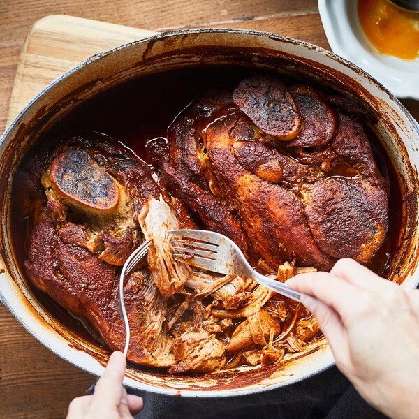 Mains en train d'effilocher le porc cuit qui se trouve dans un grand plat à cuisson. 