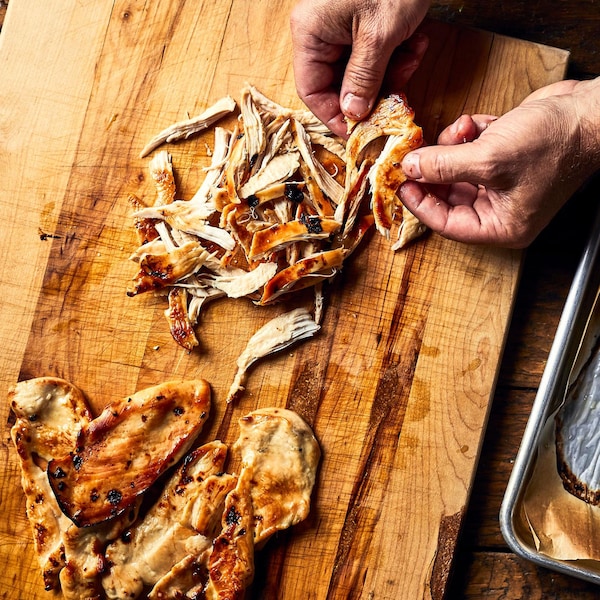 Deux mains effilochant des poitrines de poulet cuites. 