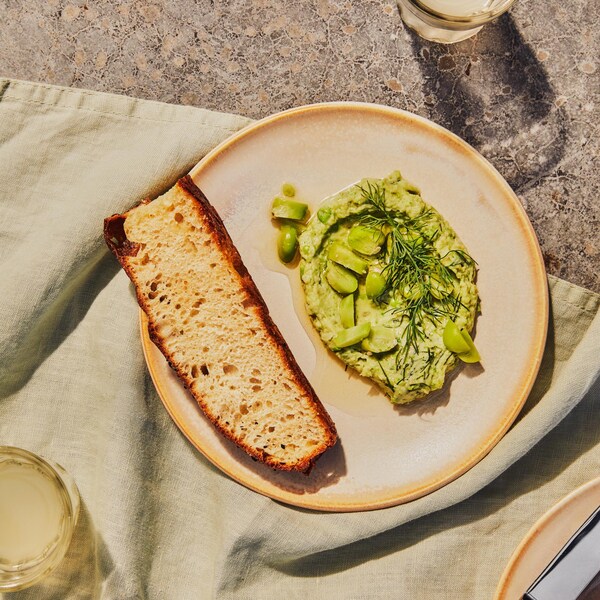 Dans une assiette, il y a de la purée de gourganes fraîches avec un croûton de pain.