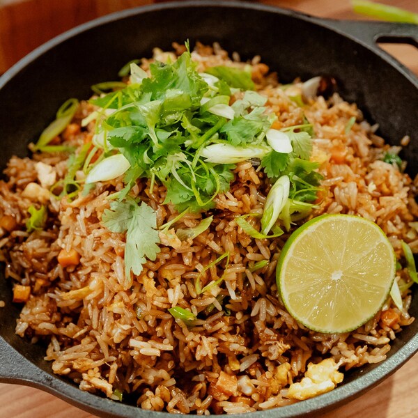 Une marmite de riz frit aux œufs garni de coriandre fraîche, d'oignons verts ciselés et d'une moitié de lime.
