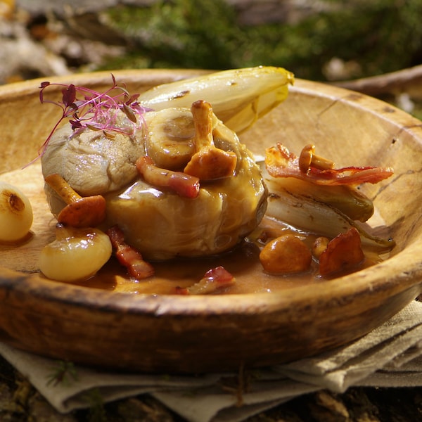 Rouelles de jarret avec des champignons, des endives et des petits oignons dans un bol en bois.