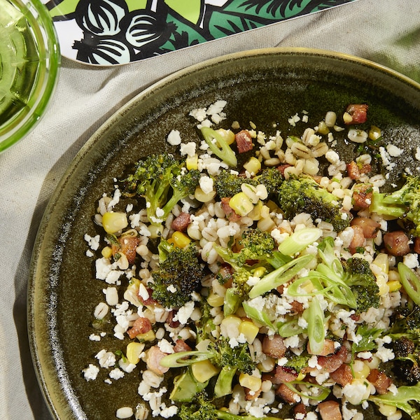 Un plat de salade de brocoli, bacon, maïs, orge et feta sur une table.