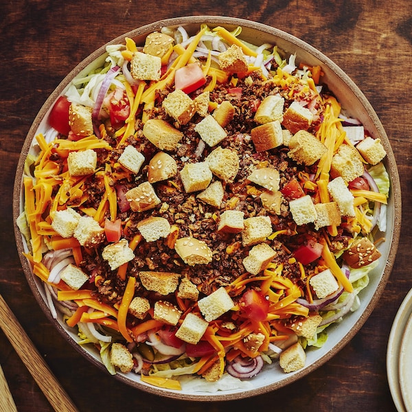 Un grand bol de salade cheeseburger avec un petit bol de sauce Big Mac maison et une pile d’assiettes.
