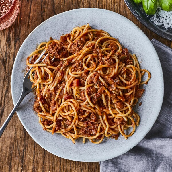 Une assiette de spaghetti avec un verre d’eau pétillante et un bol de parmesan. 