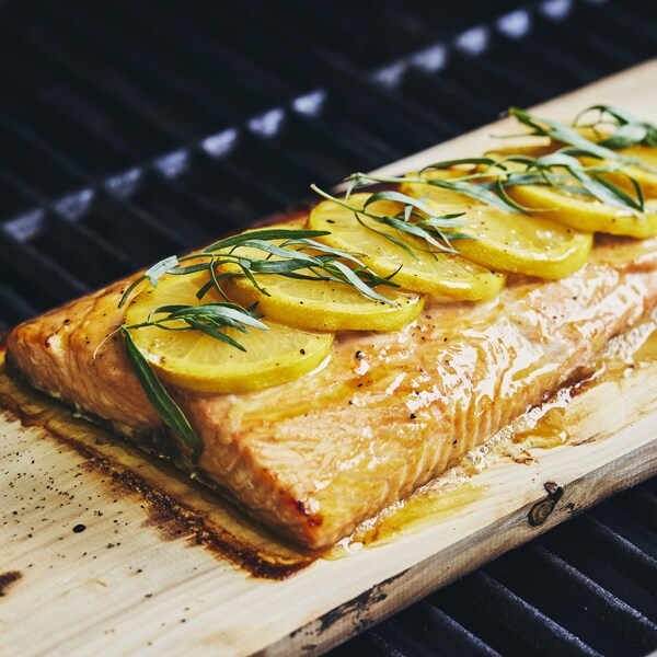 Un filet de saumon recouvert de tranches de citron sur une planche de cèdre dans un barbecue.
