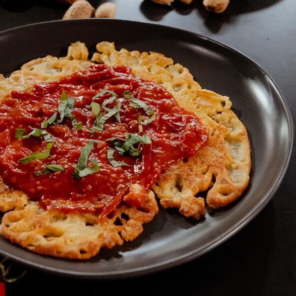 Une crêpe socca recouverte d'une compote de tomates cerises dans une assiette.