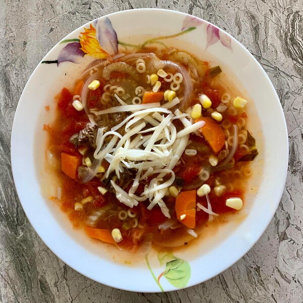 Une soupe au bœuf et légumes dans un bol avec du fromage râpé sur le dessus.