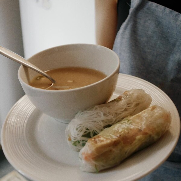 Un bol de soupe miso accompagné de deux rouleaux de printemps dans une assiette blanche.